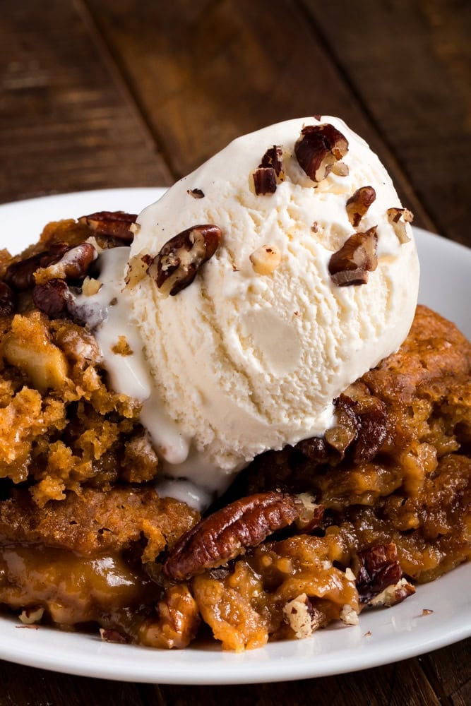 serving of sweet potato pecan pie cobbler topped with vanilla ice cream and bits of pecan.