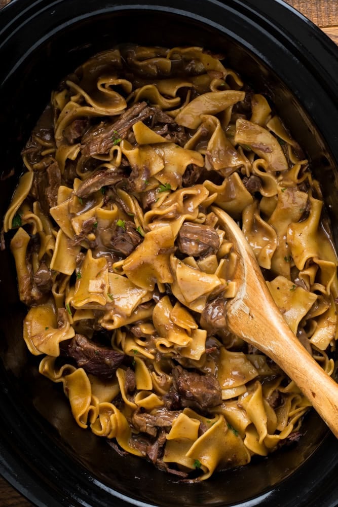 crockpot beef and noodles in slow cooker with a spoon