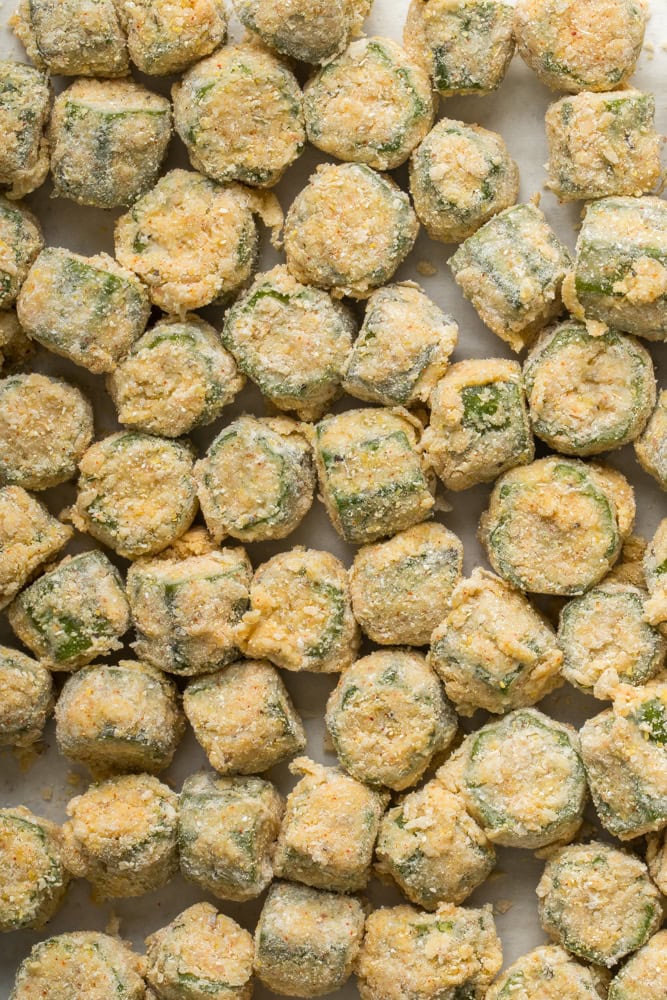 Breaded okra resting on parchment paper while the frying oil heats.