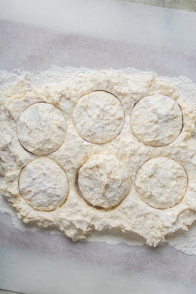 Sticky 7UP biscuit dough dusted with flour and cut into rounds on a sheet of parchment paper.