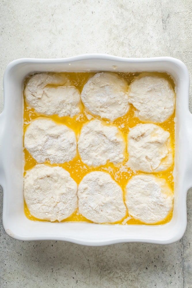 Nine unbaked 7UP biscuits arranged in a white baking dish filled with melted butter.