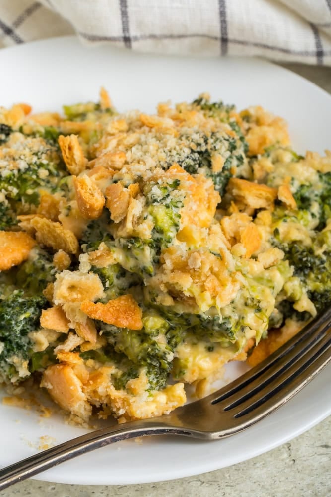 A serving of Velveeta broccoli casserole with broccoli florets in creamy cheese sauce and a golden crushed cracker topping on a white plate.