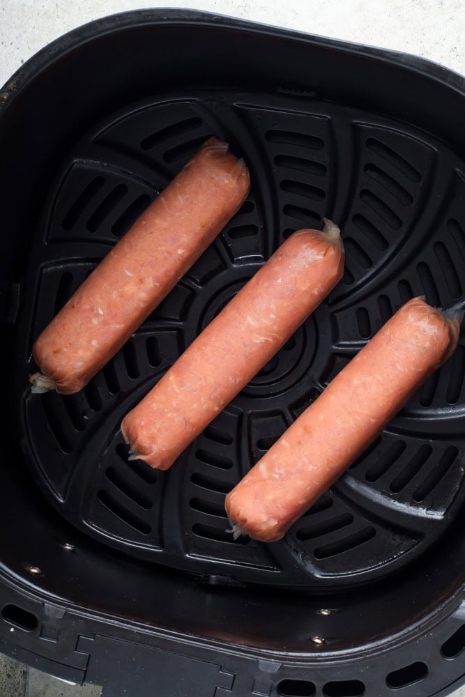 Raw chicken sausage links arranged in a single layer in the air fryer basket before cooking.