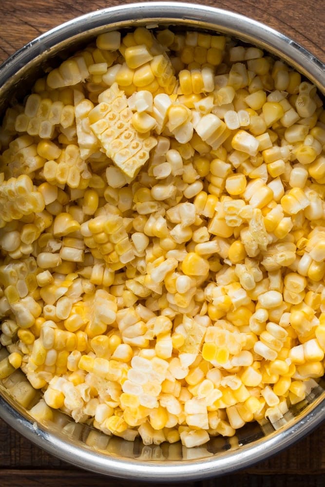 Fresh yellow and white corn kernels cut from the cob in a metal mixing bowl.