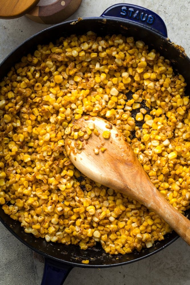 Close-up of Southern fried corn browning in a cast-iron skillet with a wooden spoon.