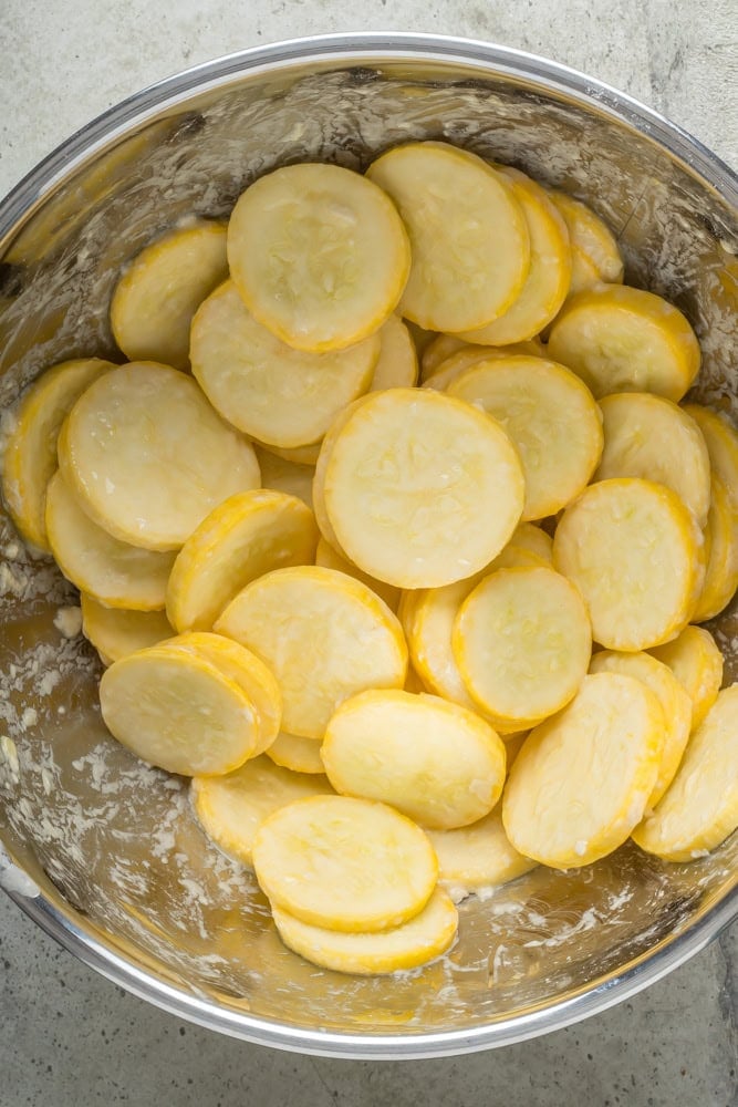 Sliced yellow squash coated in the buttermilk and egg mixture before breading.