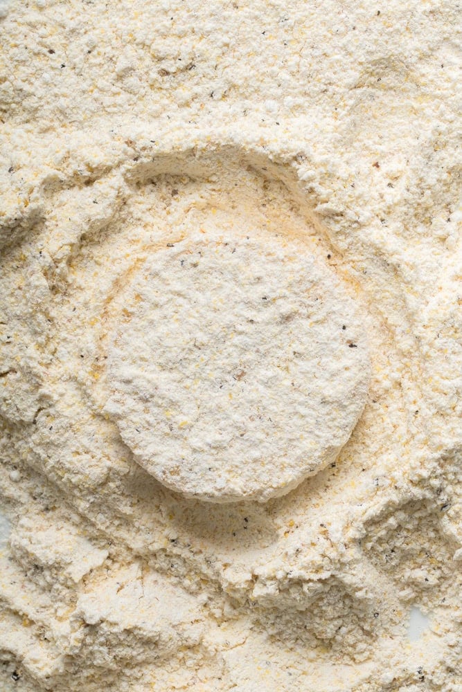 Yellow squash slice coated in seasoned flour and cornmeal breading before frying.