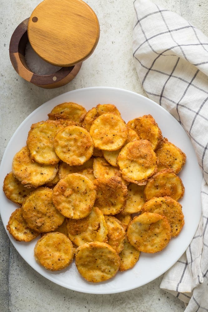 Southern fried squash rounds piled on a white plate with golden cornmeal breading and crispy edges.
