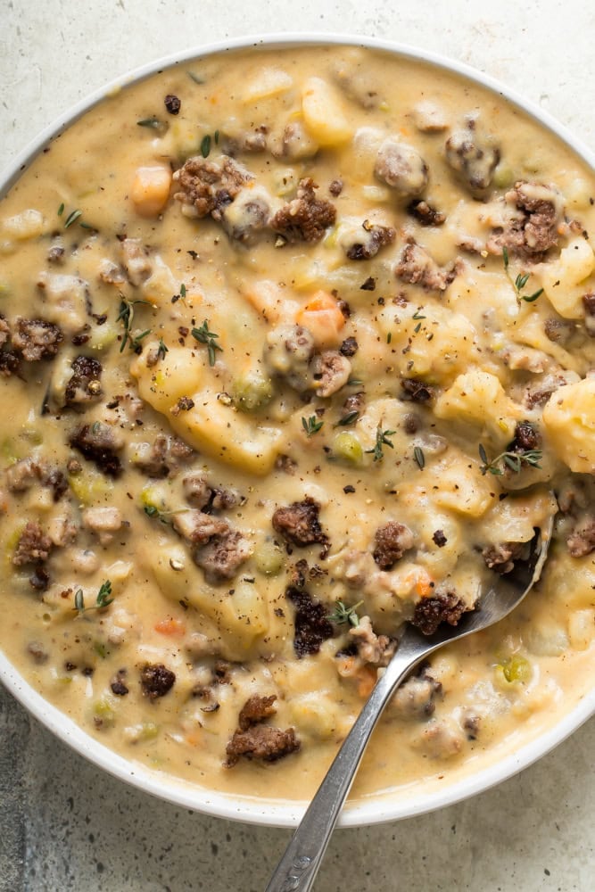Hamburger Potato Soup 1 Overhead view of creamy hamburger potato soup with browned ground beef, tender potatoes, diced vegetables, and fresh thyme in a white bowl.