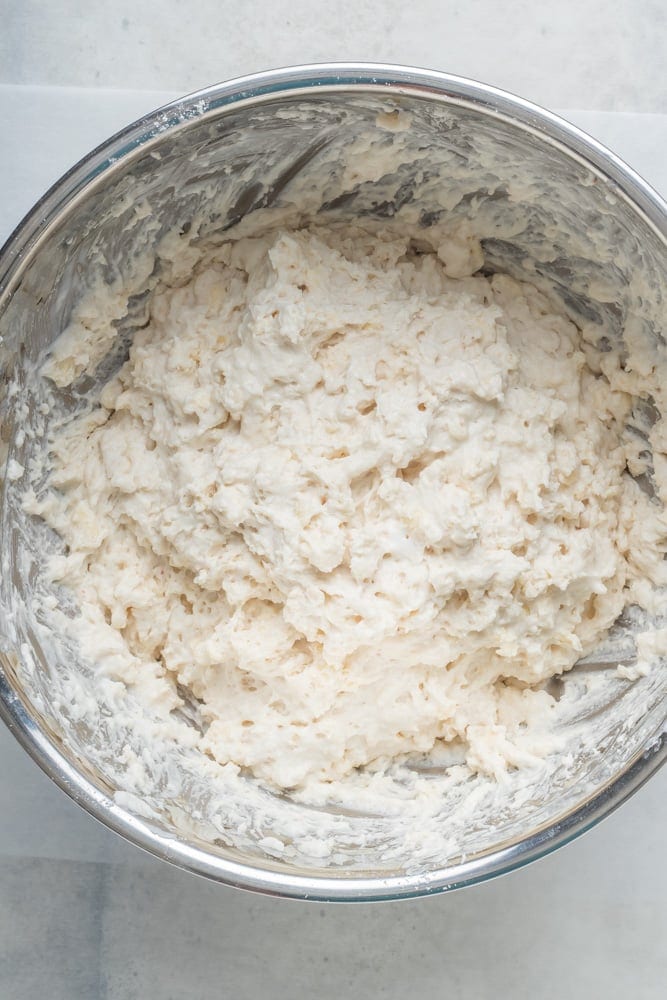 Homemade biscuit dough mixed into a shaggy consistency inside a large stainless steel bowl.