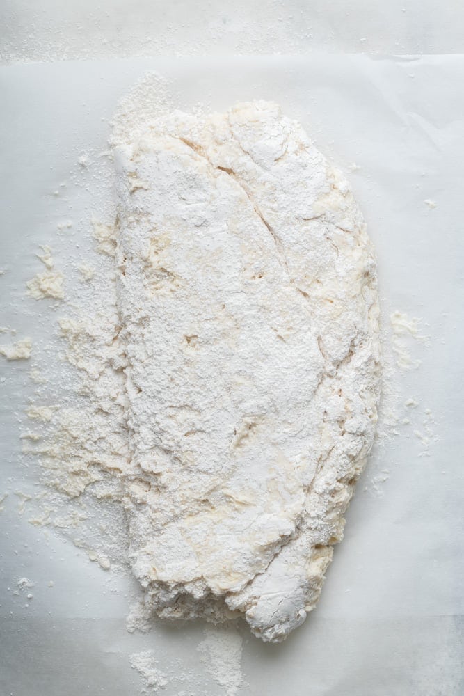 Folded homemade biscuit dough on a floured work surface before cutting into rounds.