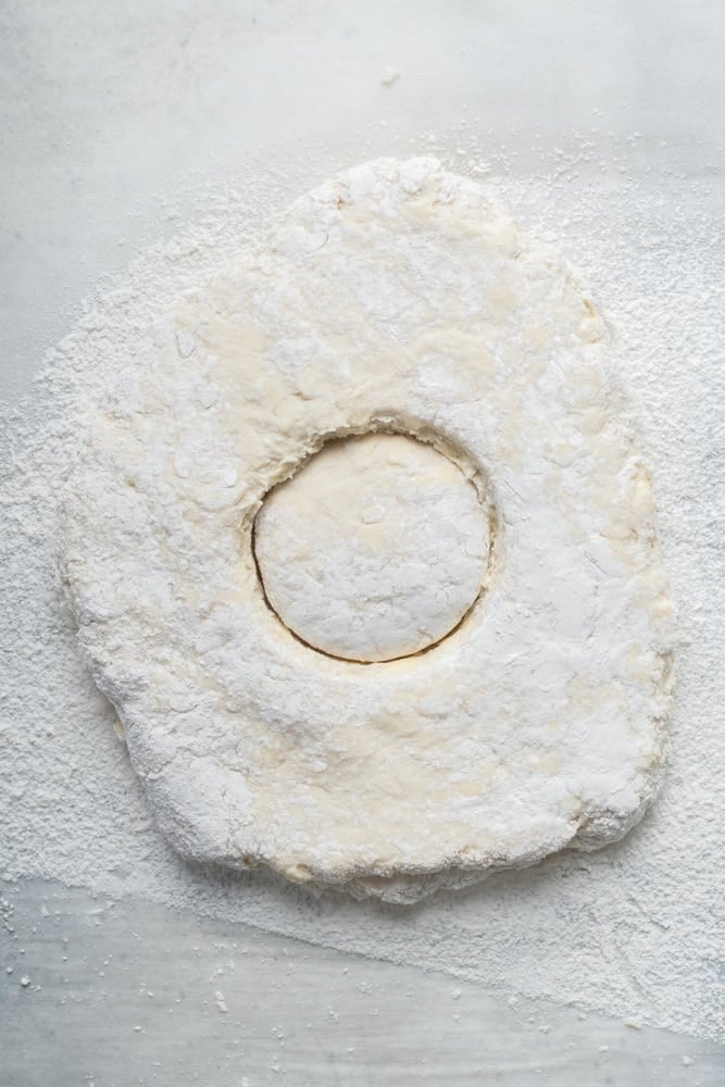Round biscuit shape cut into a thick piece of homemade dough on a floured surface.