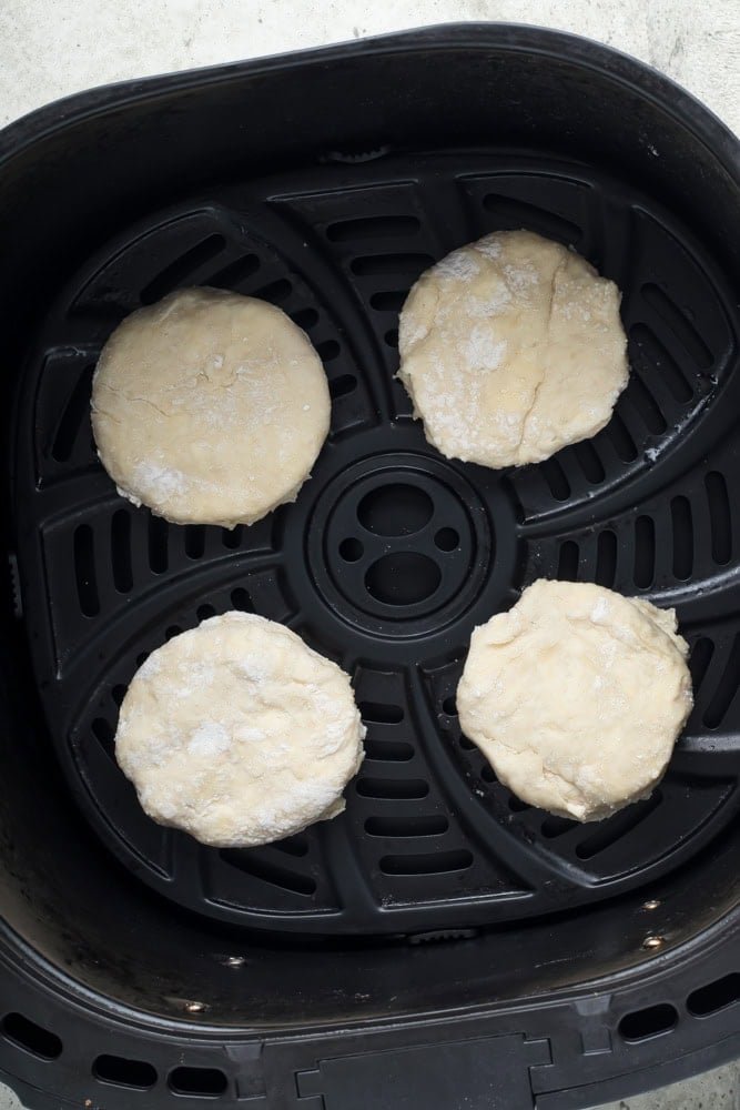Four rounds of uncooked homemade biscuit dough spaced apart in an air fryer basket.