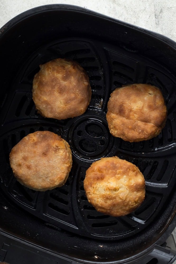 Four homemade biscuits with browned tops inside a black air fryer basket after cooking.