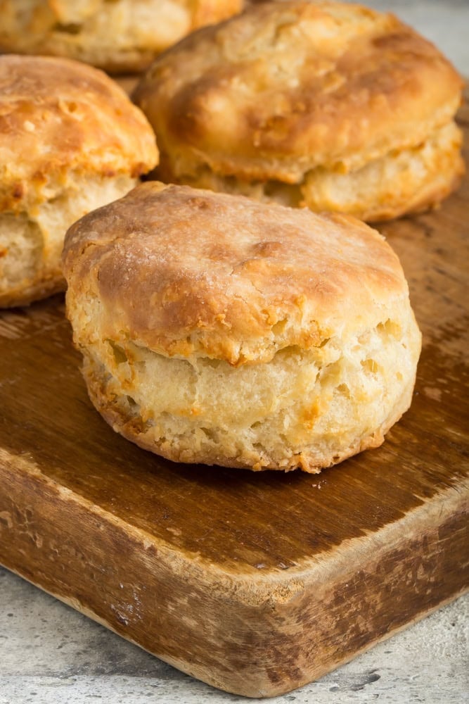 Golden-brown homemade air fryer biscuits on a wooden cutting board, showing their thick sides and layered texture.
